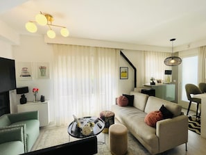 A modern living room with a sofa, armchairs, a coffee table, a TV, and a staircase.