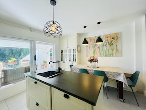 A modern kitchen with a central island, pendant lights, and a dining area with chairs.