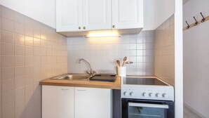 Kompakti keittiö, jossa on valkoiset kaapit, ruostumattomasta teräksestä valmistettu allas, puinen työtaso ja sisäänrakennettu uuni.