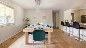 Un comedor moderno con una mesa de madera preparada para cuatro personas, sillas verdes y una barra con taburetes.