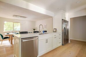 A modern kitchen with a built-in dishwasher, stainless steel appliances, and a dining area with a view of the outdoors. - Majestic Redwoods, Pool, Hot Tub, Chefs Kitchen (Sonoma)