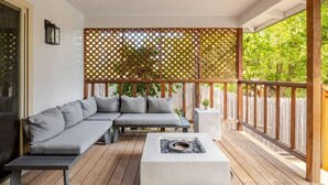Un área de estar al aire libre con techo, que incluye un sofá, una mesa baja, un brasero y un cerco de madera.