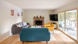 Una sala de estar moderna con chimenea, un sofá, un televisor y un balcón con mobiliario exterior.