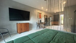 A modern bedroom with a large bed, a TV mounted on the wall, a wooden cabinet, and a dining area with chairs and a table. - Tulum Ayook apartment with Starlink (Tulum)