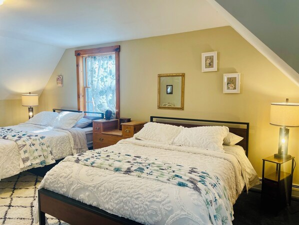 Un dormitorio con dos camas, una ventana con cortinas florales, un espejo y una mesita de noche pequeña.