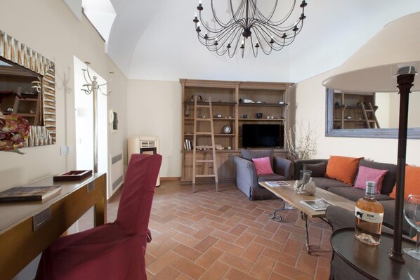Una sala de estar con televisión, sofá y una silla roja. Se observa una estantería de madera y una mesa con una botella y vasos.