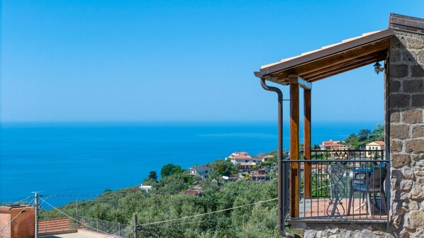 A balcony with a stone wall, overlooking a coastal town and the sea.