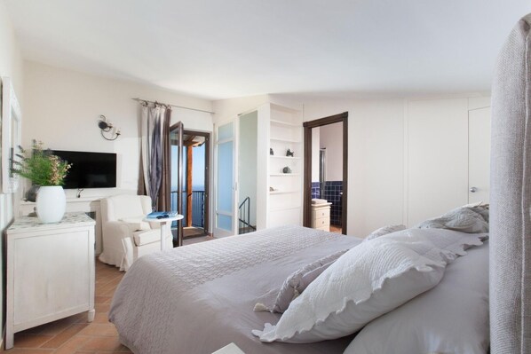 A bedroom with a bed, a desk, a chair, a TV, and a balcony.