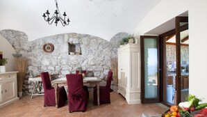 Comedor con pared de piedra, una araña y vistas a través de un ventanal.