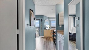 Un couloir donnant sur un balcon, un coin cuisine et un espace salon avec un canapé.
