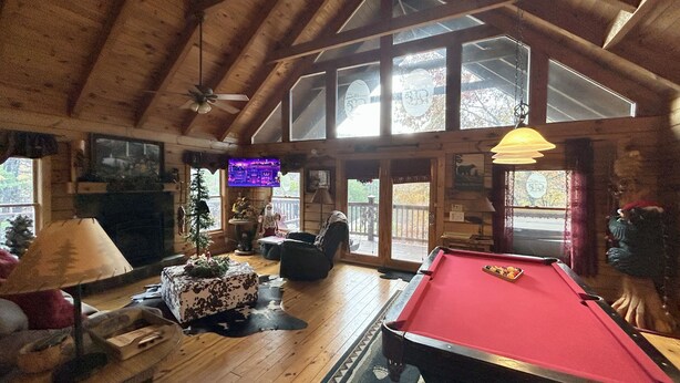 A cozy room with a pool table, wooden floors, a fireplace, and large windows. - Honeymoon log cabin with heart shaped whirlpool Tub & Hot Tub on Covered Porch (Sevierville)