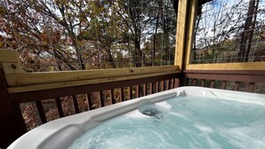 A hot tub with a wooden deck and a view of trees. - Honeymoon log cabin with heart shaped whirlpool Tub & Hot Tub on Covered Porch (Sevierville)