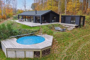 A modern house with a swimming pool, deck, and outdoor seating area surrounded by trees.