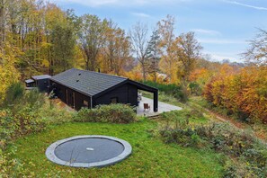 A modern cabin with a deck, surrounded by autumn foliage.