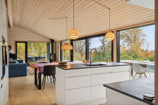 A modern kitchen with a central island, large windows, and a dining area with a blue sofa. - Wonderful holiday home with sea view (Asnæs)