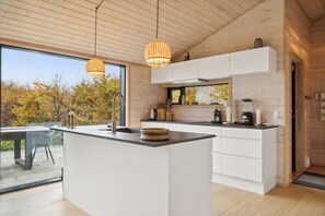 A modern kitchen with a large island, pendant lights, and a view of autumn trees. - Wonderful holiday home with sea view (Asnæs)