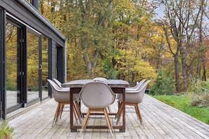 En træterrasse med et bord og stole, omgivet af træer med efterårsfarver.