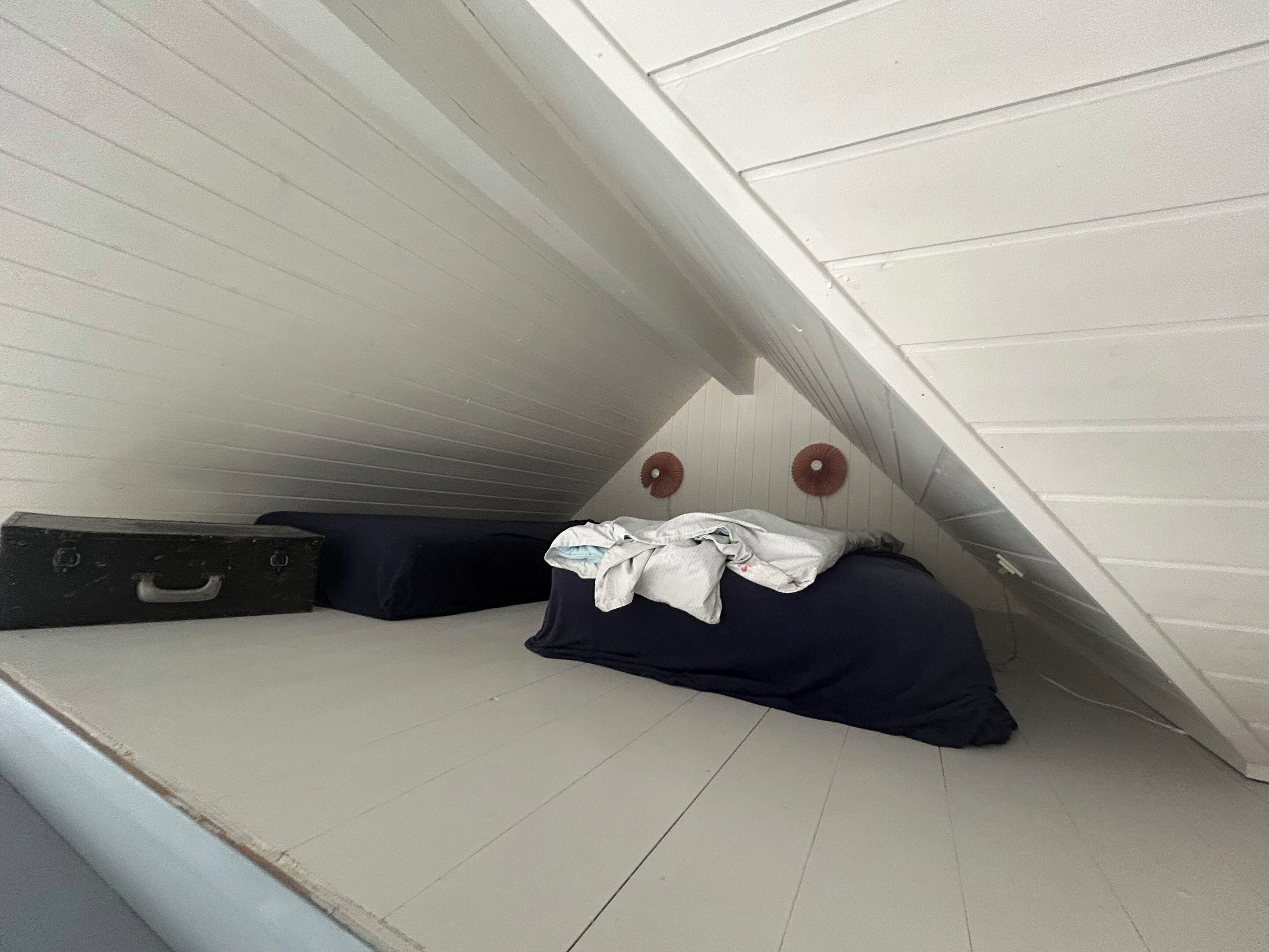 A small attic bedroom with a sloped ceiling, a single bed, a suitcase, and a wall-mounted light fixture.
