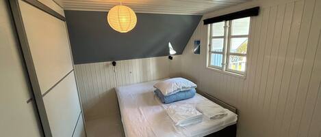 A bedroom with a bed, a window, a wall-mounted light fixture, and a door.