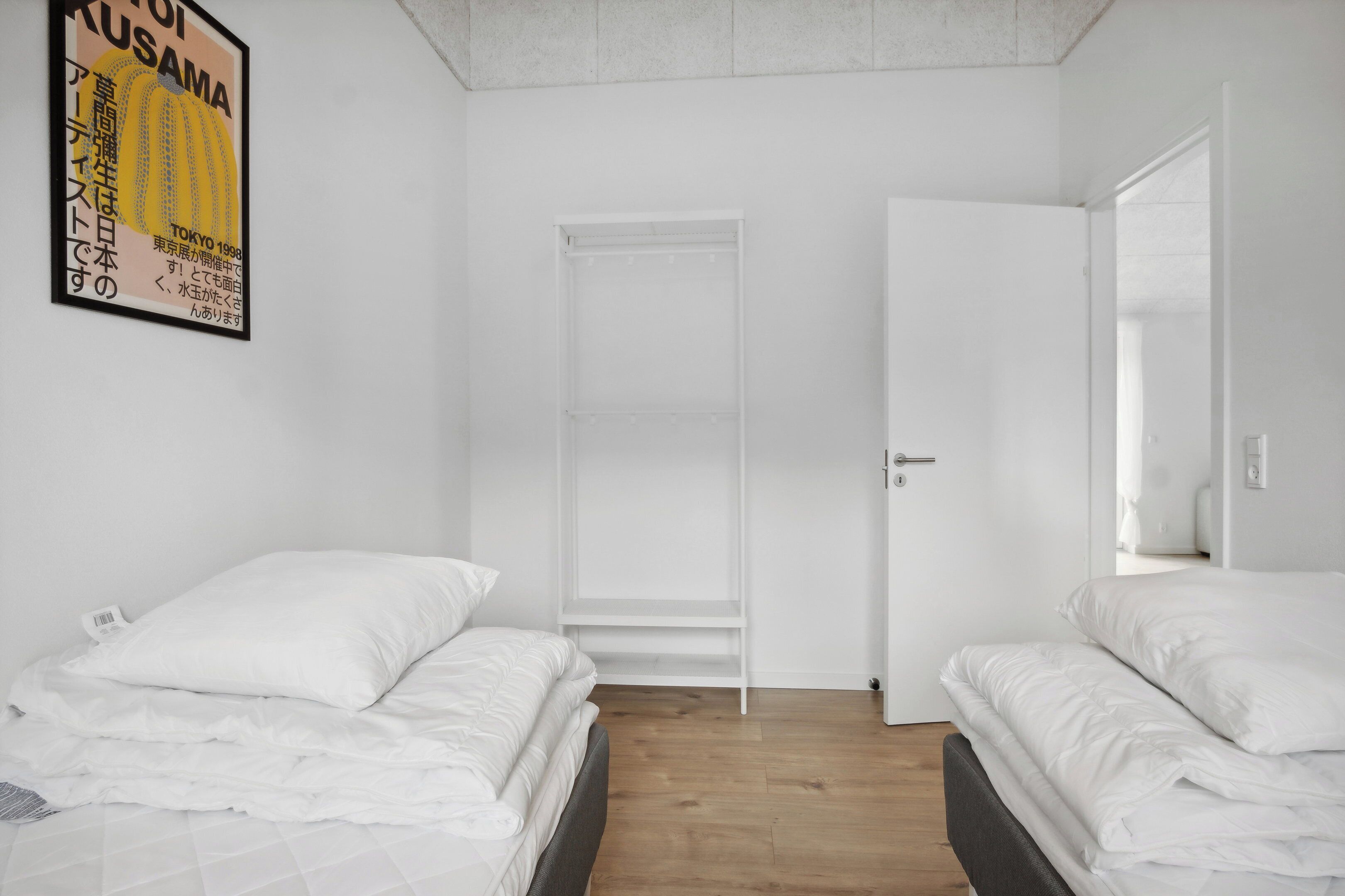 A bedroom with two beds, a wardrobe, and a door leading to another room.