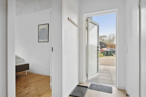 A hallway with a bed, a framed picture, a door leading outside, and a mat at the door's entrance.