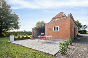 A brick house with a patio, a barbecue grill, and a small table with chairs.