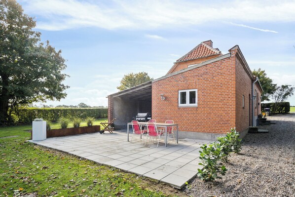 A brick house with a patio, a barbecue grill, and a small table with chairs.