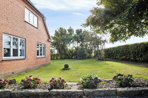 A brick house with a well-maintained lawn, a hedge, and a small tree.