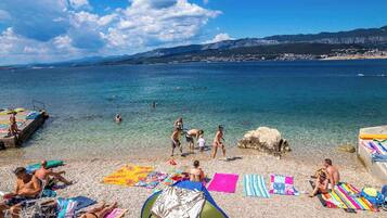 Ein Strand mit badenden und sonnenden Personen, einem Zelt und einer felsigen Küstenlinie.