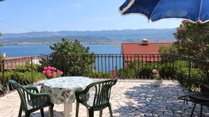 Una terraza con mesa y sillas, vista al mar y un edificio de techo rojo al fondo.