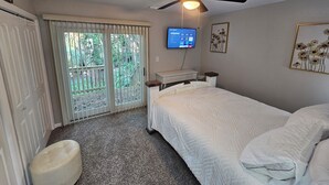 Une chambre avec un lit, un ventilateur de plafond, un téléviseur fixé au mur et une fenêtre donnant sur un paysage verdoyant.