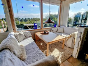 A cozy room with a sofa, a table, and a view through large windows. - 3 bedroom accommodation in Roslev (Roslev)
