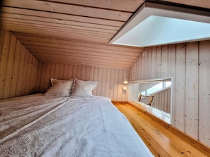 A bedroom with a sloped ceiling, wooden walls, a bed with a patterned bedspread, a nightstand, and a skylight. - 3 bedroom accommodation in Roslev (Roslev)