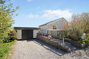 A residential property with a gravel driveway, a wooden fence, and a stone wall with flowers.