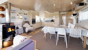 Une cuisine chaleureuse avec un poêle à bois, des chaises blanches et une table à manger.