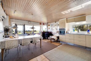 A modern kitchen with wooden ceiling, a dining area with chairs, and a view through the window. - 3 bedroom accommodation in Roslev (Roslev)