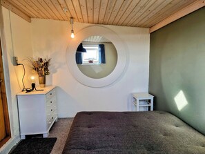 Ein Schlafzimmer mit einem runden Spiegel, einem Nachttisch mit Lampe, einer Kommode und einem kleinen Hocker.