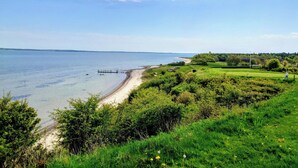 Un paysage côtier avec une plage, des zones herbeuses et un ciel dégagé.
