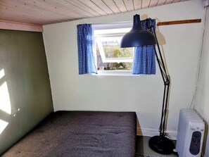 A small room with a single bed, a window with blue curtains, a desk lamp, and a heater. - 3 bedroom accommodation in Roslev (Roslev)