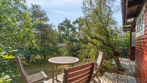 Eine Holzterrasse mit Tisch und Stühlen, umgeben von Bäumen und einer Ziegelmauer.