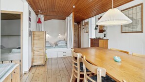 Ein Zimmer mit Holzboden, einem Esstisch mit Stühlen, einem Bett mit Holzvorhang und einer roten Pendelleuchte. An der Wand hängt eine Karte.