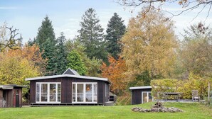 Une maison moderne dotée de grandes fenêtres, d’un porche abrité et d’une cheminée en pierre.