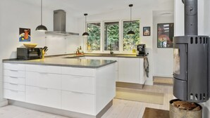 Une cuisine moderne avec des meubles blancs, un îlot central, des luminaires suspendus, une cuisinière et de grandes fenêtres.