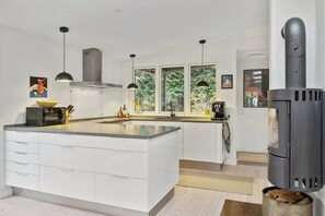 Cocina moderna con armarios blancos, una isla central, iluminación colgante, una estufa y ventanas amplias.
