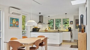 Une cuisine moderne avec des meubles blancs, un îlot central, des luminaires suspendus et des œuvres d’art accrochées aux murs.