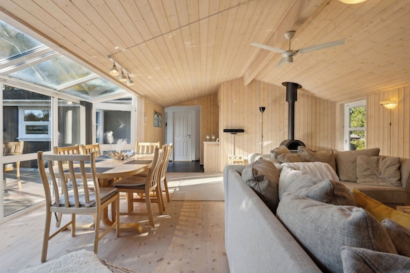Un vaste espace de vie dotĂ© de planchers en bois, dâun canapĂ©, dâune table Ă manger, de chaises et dâun ventilateur de plafond.