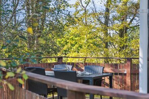 Une terrasse dotĂ©e de mobilier dâextĂ©rieur, entourĂ©e dâune clĂŽture en bois et dâarbres.