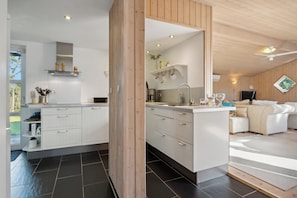 Une cuisine moderne avec des meubles blancs, un ßlot central et un coin repas comprenant un canapé et une table basse.