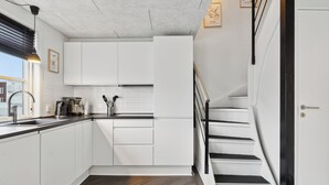 Une cuisine moderne avec des meubles blancs, un plan de travail noir et un escalier doté de rampes noires.