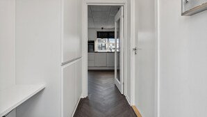 Un couloir menant à une cuisine dotée de meubles blancs et d’un parquet disposé en motif à chevrons.